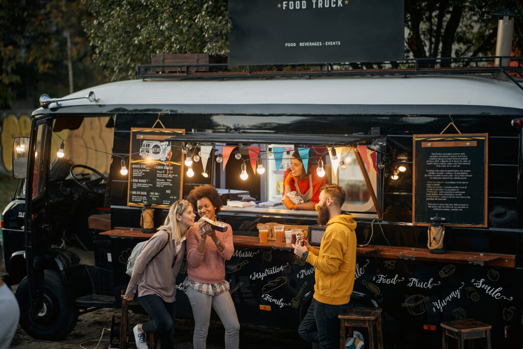 multiethnic group of young people socializing while eating outdoor in front of modified truck for fast food