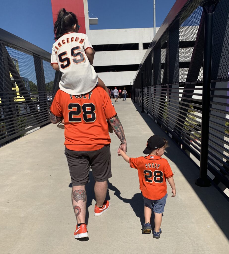 Erik walking with his two kids while wearing orange sports jerseys