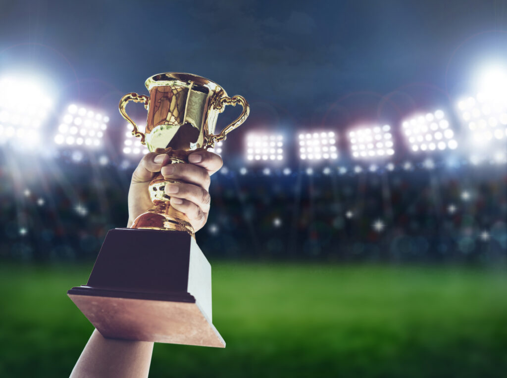 Man holding up a a gold trophy cup is winner in a competition in night stadium.