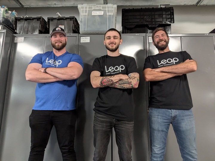 Three warehouse employees in Leap Event Technology shirts, smiling for a photo