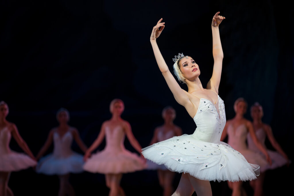 Prima ballerina white swan on stage dancing gracefully against other dancers