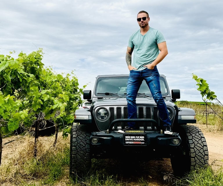 joe standing on a jeep in a vineyard