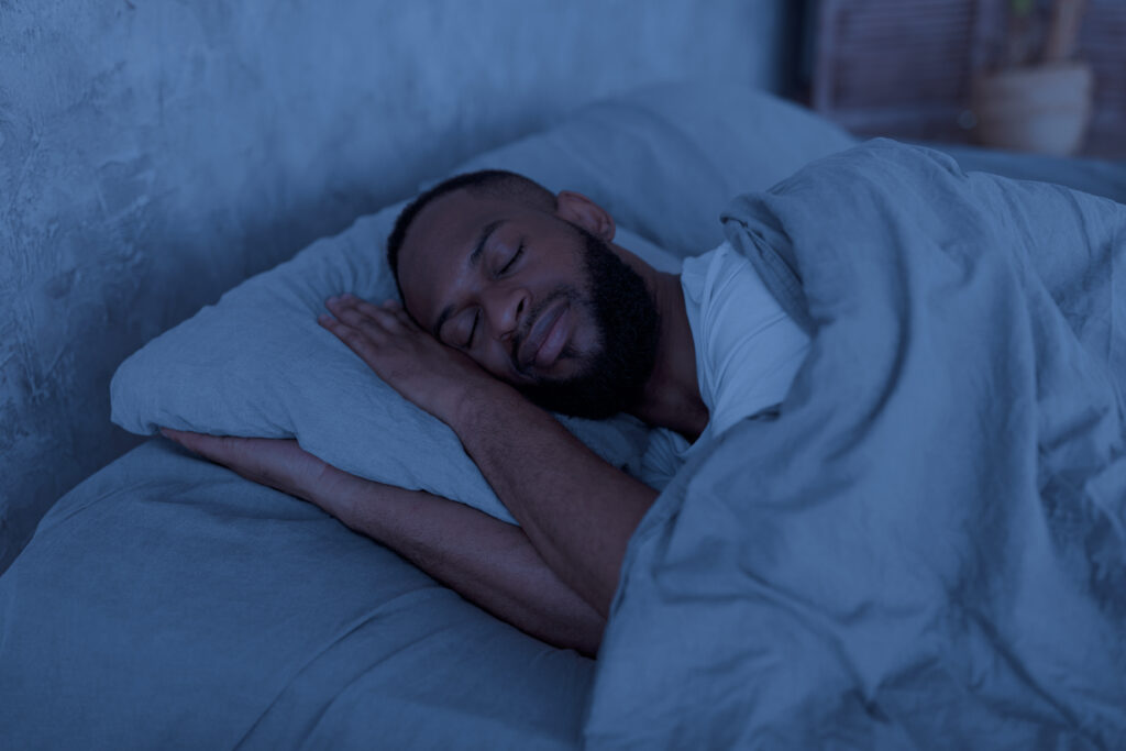 happy young well-slept African American man lying in bed with closed eyes