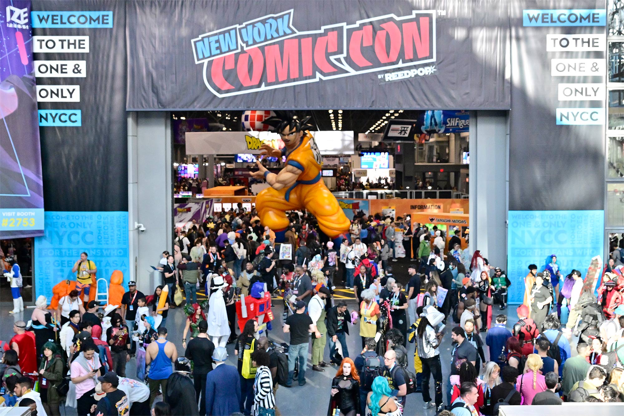 The entryway of New York Comic Con with a crowd of attendee swarming the front. There is a large statue of Son Goku from Dragon Ball near the center.