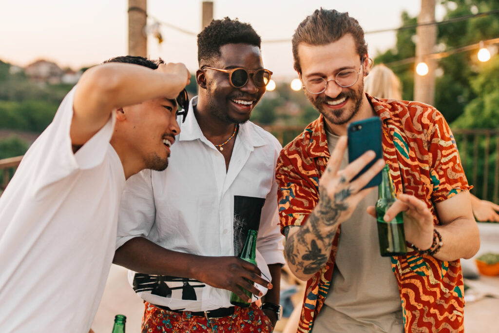 Three multiracial hipster friends are smiling at the phone while looking at photos