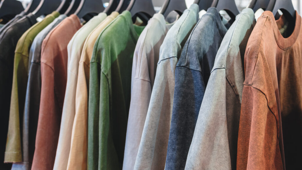 A row of shirts hanging on a rack, with some being green and others being brown. The shirts are all different colors and styles, and they are all hanging on the same rack